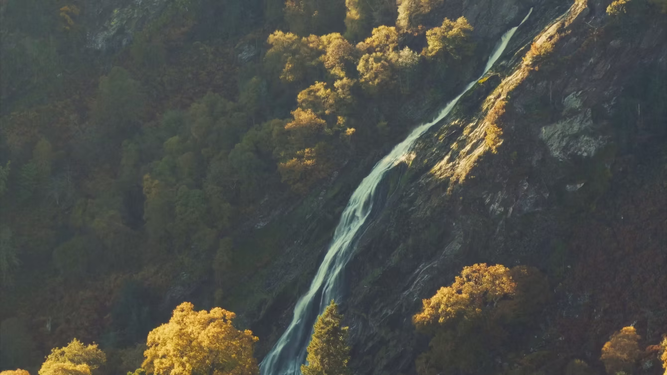 Waterfall running down a wooded slope in autumn colour
