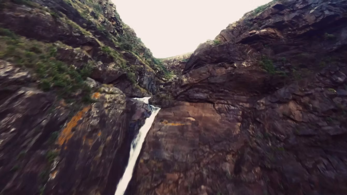 FPV drone descent alongside a waterfall in a rocky gorge